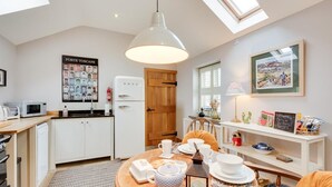 Une cuisine moderne avec des meubles blancs, un réfrigérateur blanc et une table à manger en bois, mise avec des tasses à thé et une théière.