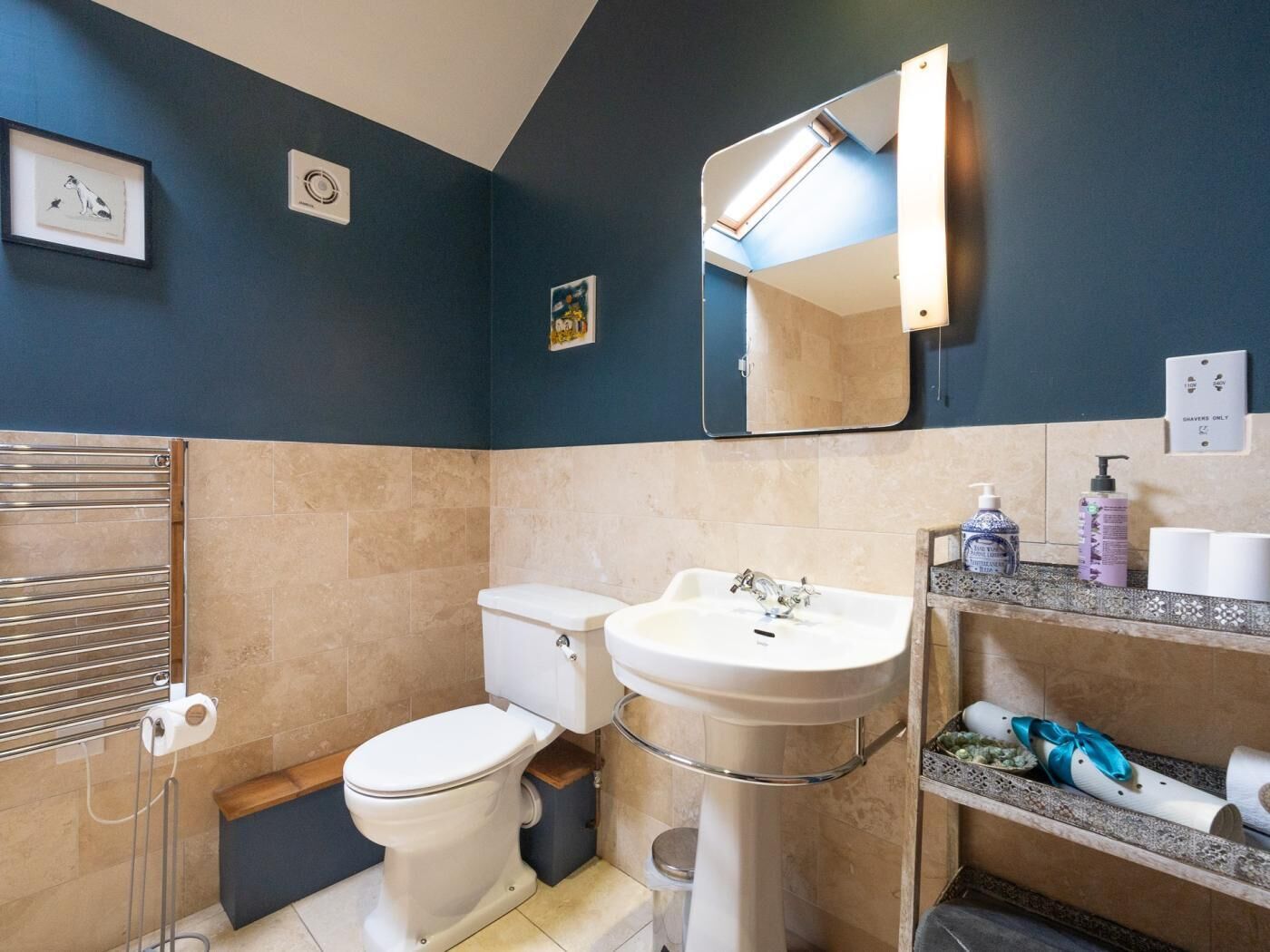Une salle de bain équipée d’un WC, d’un lavabo, d’un miroir, d’un porte-serviettes et d’une étagère contenant des articles de toilette.