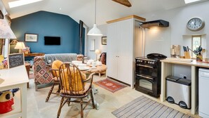 Une cuisine chaleureuse avec un poêle, un coin repas avec une table et des chaises, un mur bleu et une chambre en mezzanine avec un lit.