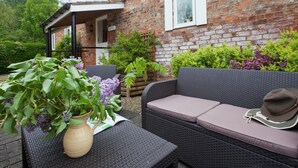 Eine Terrasse mit Korbmöbeln, einem Blumentopf und einem Backsteinhaus im Hintergrund.