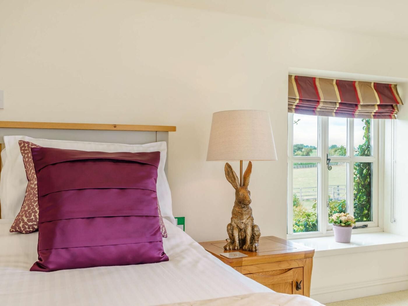 Una cama con cabecera, una lámpara con diseño de conejo y una ventana con vistas a zonas verdes.