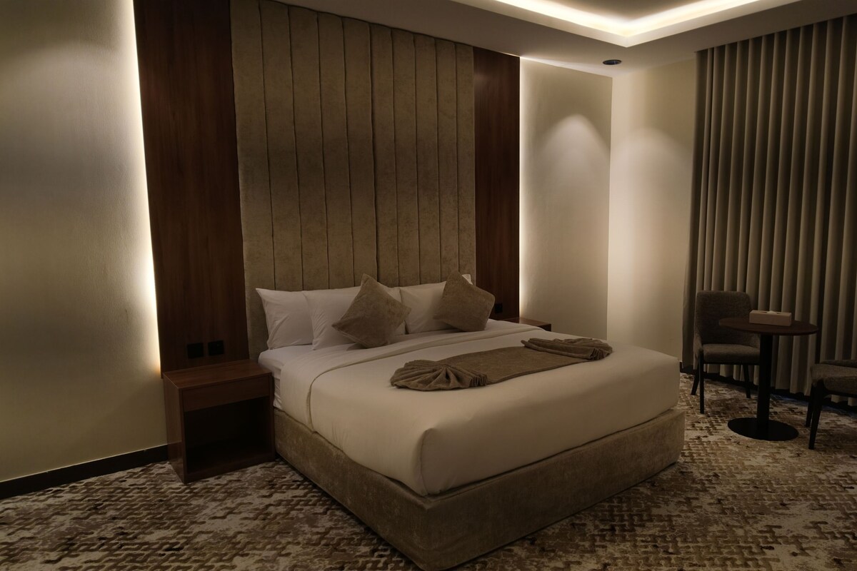 Una habitación de hotel con una cama grande, una mesita de noche, una silla y una pequeña mesa.