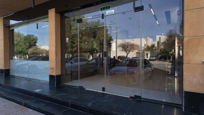 A building entrance with glass doors, a sign indicating an exit, and a reflection of parked cars. - Sahat Al Khaleej Serviced Apartments (Riyadh)
