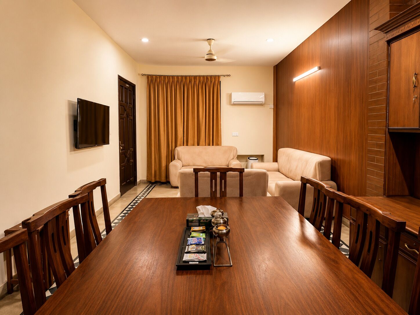 A conference room with a wooden table, chairs, a sofa, and a television on the wall.