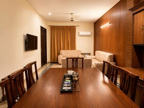 A conference room with a wooden table, chairs, a sofa, and a television on the wall.