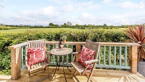 A wooden deck with two chairs and a table, overlooking a vineyard. - 2 Bed in Llanfairpwllgwyngyll (oc-82559) (Brynsiencyn)