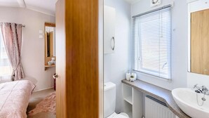A bedroom with a bed, a wooden door, and a bathroom with a sink, toilet, and window blinds. - 2 Bed in Llanfairpwllgwyngyll (oc-82559) (Brynsiencyn)