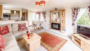 A modern living room with a sofa, coffee table, TV, fireplace, dining area, and kitchen. - 2 Bed in Llanfairpwllgwyngyll (oc-82559) (Brynsiencyn)