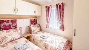 A bedroom with two beds, a wardrobe, and a window with curtains. - 2 Bed in Llanfairpwllgwyngyll (oc-82559) (Brynsiencyn)