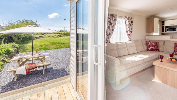 A modern RV with a sliding door, a dining area with a table and chairs, a sofa, and a kitchen area with a microwave. - 2 Bed in Llanfairpwllgwyngyll (oc-82559) (Brynsiencyn)