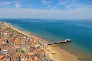 An aerial view of a coastal town with a beach, a pier, and a mix of residential and commercial buildings. - 4 Bed in Cromer (oc-82588) (Cromer)