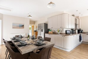 A modern kitchen with a central island, white cabinetry, and a dining area with a table set for six. - 4 Bed in Cromer (oc-82588) (Cromer)