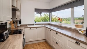 A modern kitchen with white cabinets, a wooden countertop, a sink, and a window with a view of greenery. - 4 Bed in Cromer (oc-82588) (Cromer)