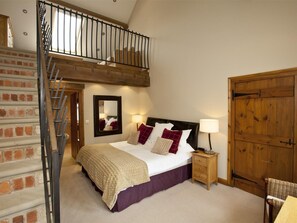 Ein Schlafzimmer mit einem Bett, einem Nachttisch, einem Holzschrank, einem Spiegel und einer Treppe.