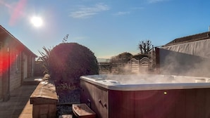 Ein Whirlpool in einer sonnigen Außenanlage mit einem Steinweg und einem Holzzaun.