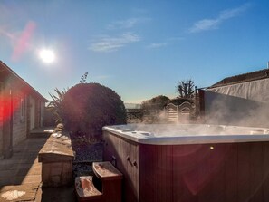 Ein Whirlpool in einer sonnigen Außenanlage mit einem Steinweg und einem Holzzaun.
