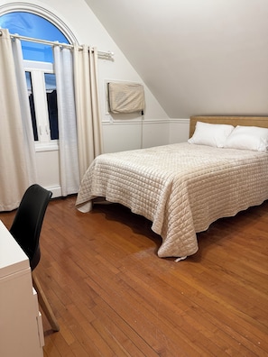 A bedroom with a bed, a desk, a window with curtains, and a view of the sky.