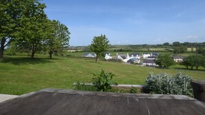 Un paysage rural avec une rangée de maisons blanches, un grand arbre et un champ d’herbe.