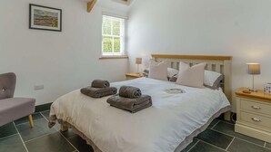 Une chambre à coucher avec un grand lit, deux tables de chevet, une chaise, une fenêtre et un tableau au mur.
