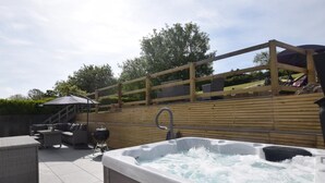 Un bain à remous, du mobilier d’extérieur et une terrasse en bois offrant une vue sur le ciel et les arbres.