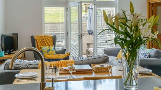 Une cuisine moderne équipée d’un évier, d’une table et de chaises, d’un téléviseur, et offrant une vue sur l’extérieur grâce à de grandes fenêtres.