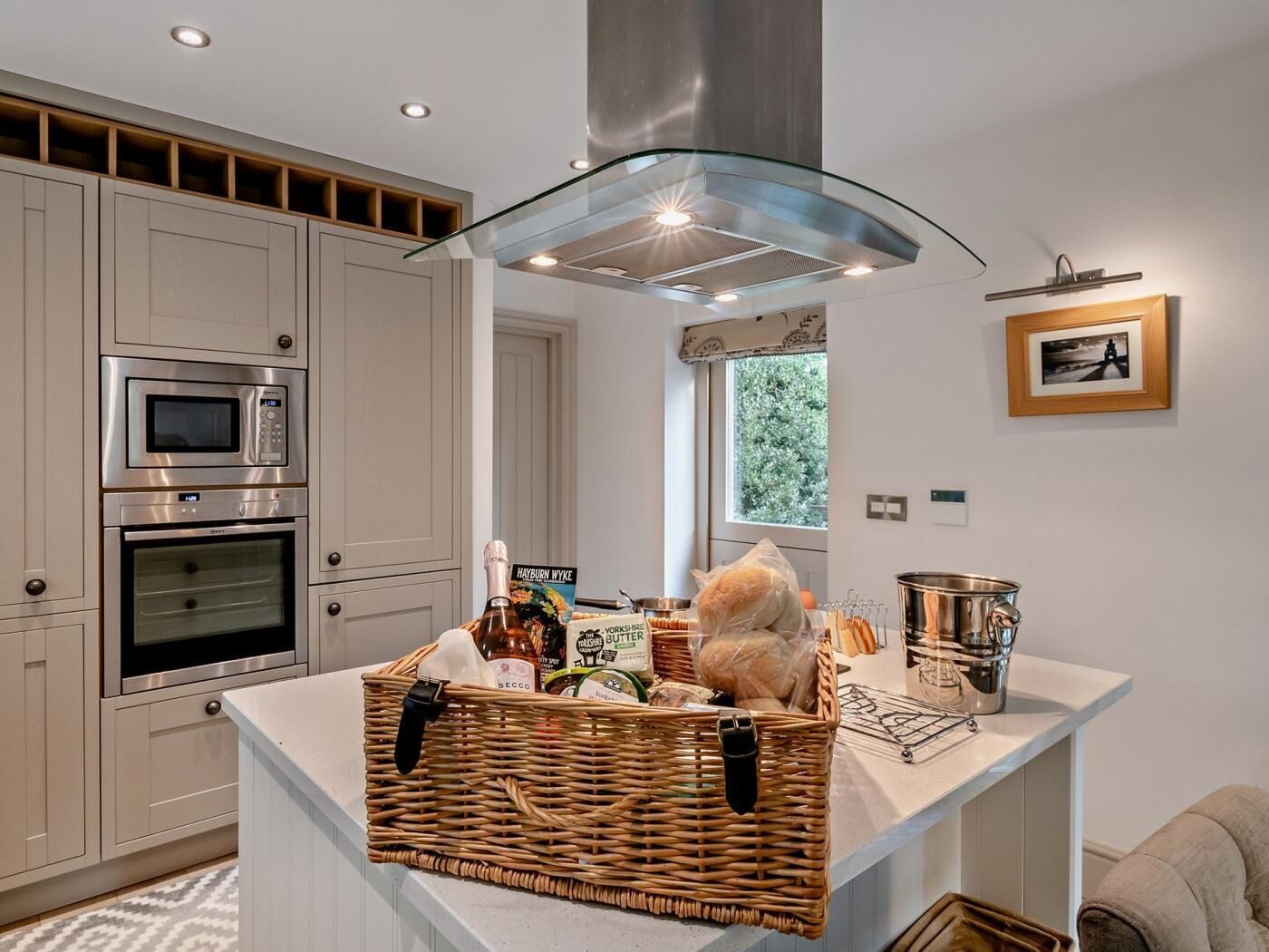 A modern kitchen with built-in appliances, a central island, and a view of greenery outside.