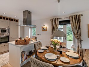 A modern kitchen with built-in appliances, a dining area with a round table, and a view of greenery outside. - 2 Bed in Scarborough (oc-g0179) (Staintondale)