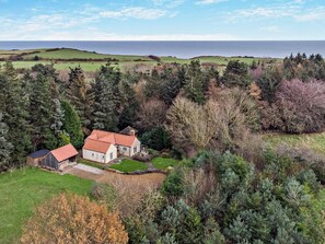 A house with a red roof, surrounded by dense trees and a view of the sea. - 2 Bed in Scarborough (oc-g0179) (Staintondale)