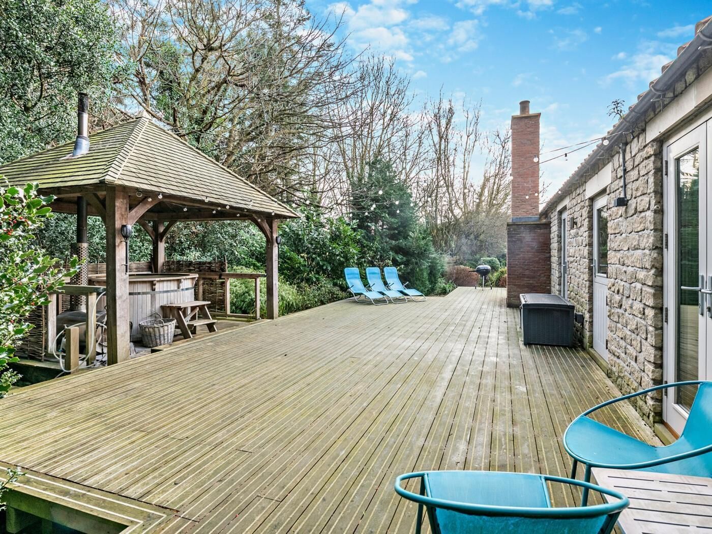 A wooden deck with lounge chairs, a barbecue area, and a stone building with a chimney.