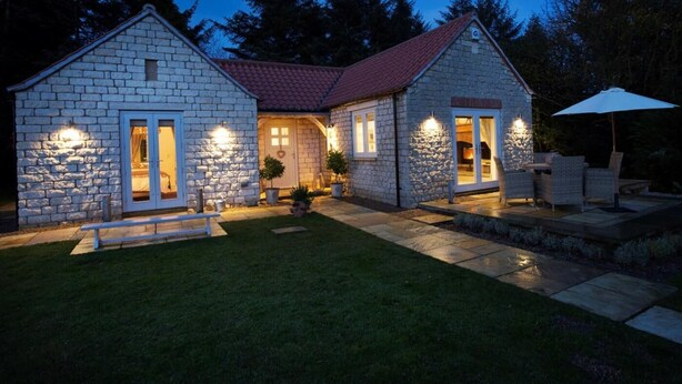 Una casa de piedra con techo rojo, un porche y un patio con mobiliario exterior.