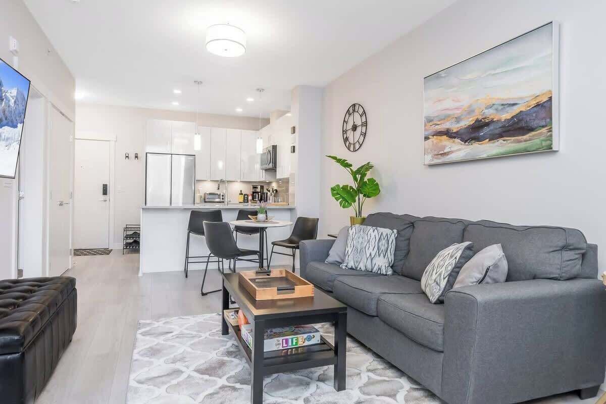 Ein modernes Wohnzimmer mit grauem Sofa, einem Couchtisch und einem Essbereich mit Stühlen.