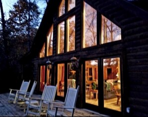 A log cabin with large windows, outdoor seating, and a visible interior with a dining area. - Stunning, huge 5 bdrm log home- Canoe/firepi!t/pet (Lake Lure)