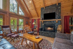 A cozy cabin interior with a stone fireplace, wooden furniture, and large windows. - Stunning, huge 5 bdrm log home- Canoe/firepi!t/pet (Lake Lure)