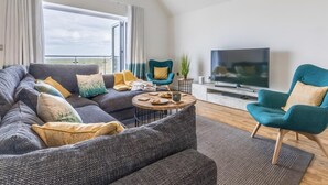 Ein modernes Wohnzimmer mit einer Couch, einem Couchtisch, einem Fernseher und einem Sessel.