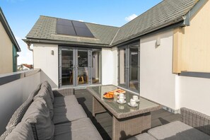 A rooftop terrace with a glass door entrance, a wicker sofa, a glass table with a fruit basket, and a solar panel. - 4 Bed in Westward Ho! (oc-74128) (Westward Ho!)