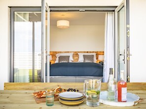 Ein Schlafzimmer mit einem Bett, einem Nachttisch mit Lampe und Blick durch eine Glastür.
