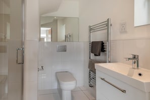 Uma casa de banho moderna com cabine de chuveiro em vidro, sanita branca, toalheiro com toalhas e lavatório com torneira.