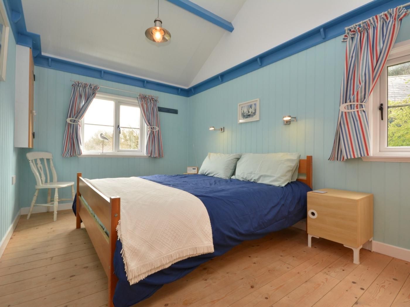 A bedroom with a bed, bedside table, chair, and a window with curtains.