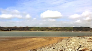 Eine Küstenlandschaft mit Strand, einem Gewässer und sanften Hügeln im Hintergrund.