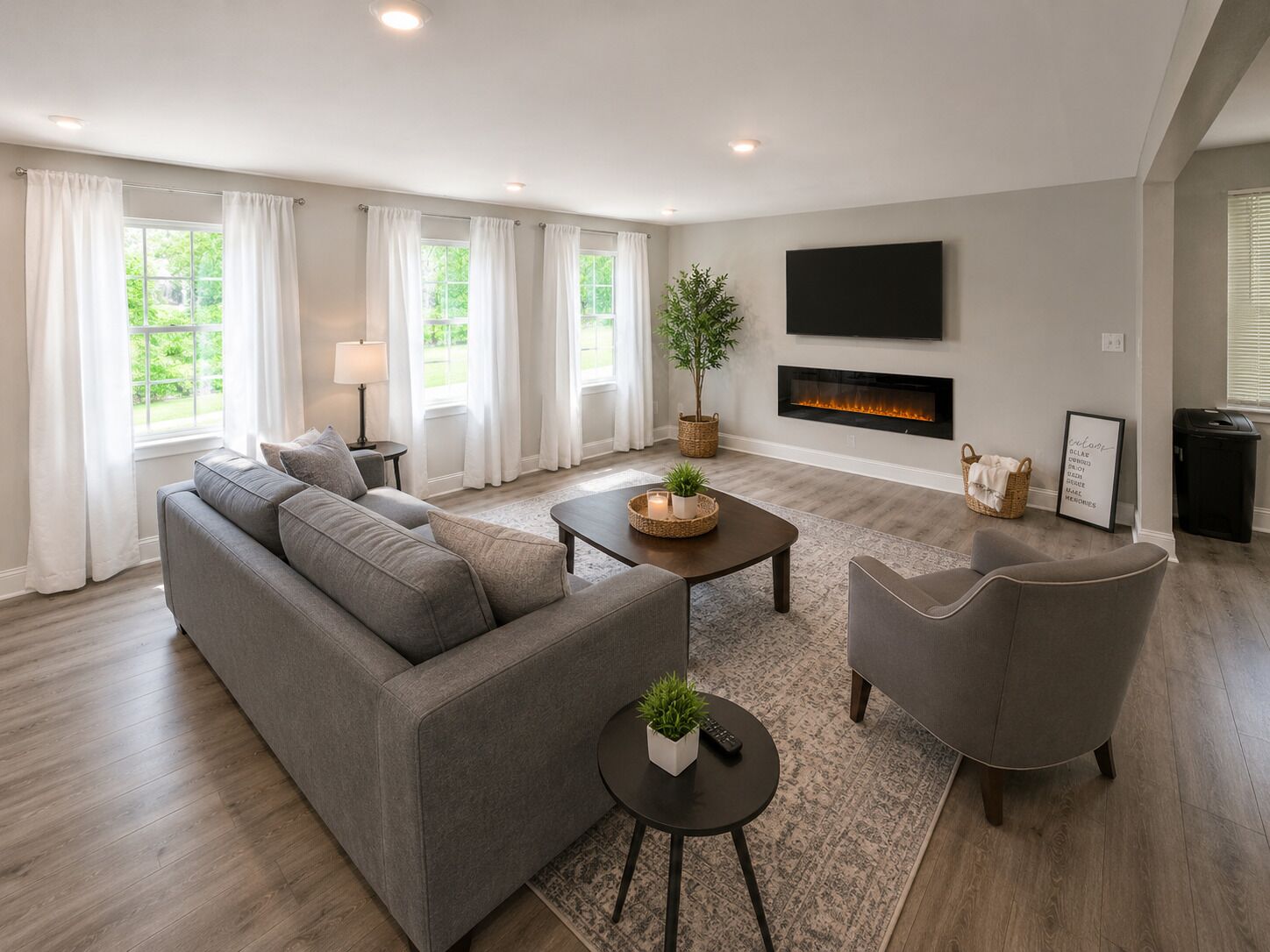 Un salon moderne avec un canapé gris, une table basse, un téléviseur fixé au mur et une cheminée.
