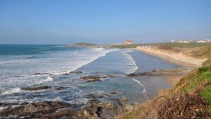 Paisatge costaner amb una platja, línia de costa rocosa i edificis a la distància.
