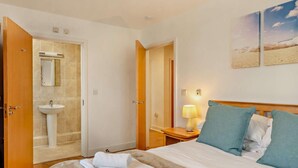 Habitació d'hotel amb llit, una làmpada de nit, un bany amb mànega i una porta que dona a una altra habitació.