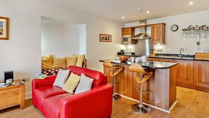 Un apartament modern amb un sofà de cuir vermell, tamborets de bar de fusta, una cuina amb armaris de fusta i una zona de menjador.