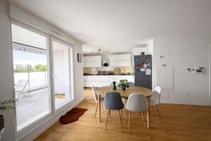 Een moderne keuken met witte kasten, een eettafel met stoelen, en een groot raam.
