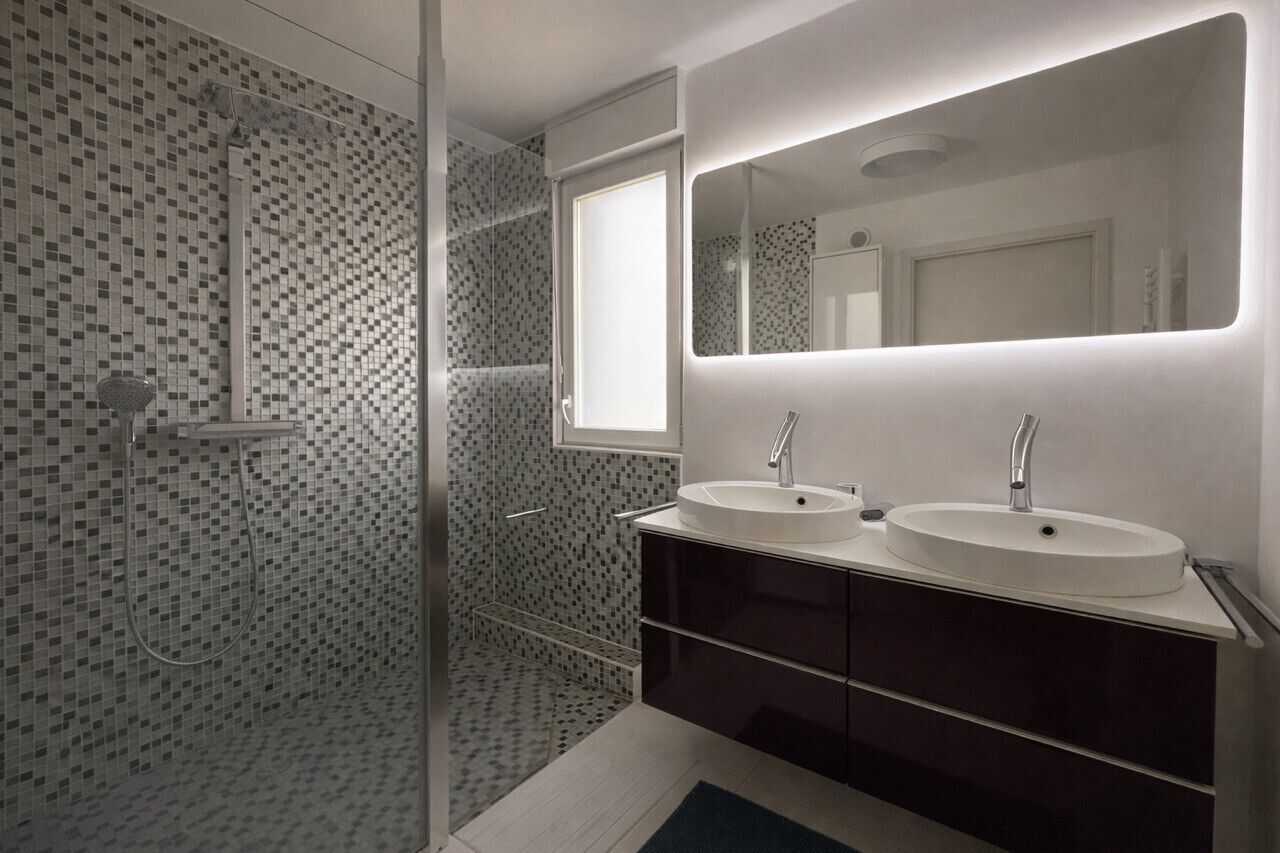 Une salle de bain moderne avec deux lavabos, un grand miroir et une douche aux carreaux de mosaïque.