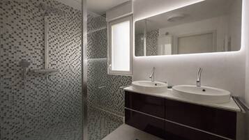 Une salle de bain moderne avec deux lavabos, un grand miroir et une douche aux carreaux de mosaïque.