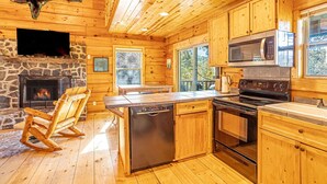 A log cabin interior with a stone fireplace, wooden flooring, a kitchen with modern appliances, and a large window. - Huge River/Mountain Views!3story log/canoes/ pet (Lake Lure)