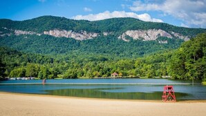 A beach with a lake, mountains, and a red lifeguard chair. - Huge River/Mountain Views!3story log/canoes/ pet (Lake Lure)