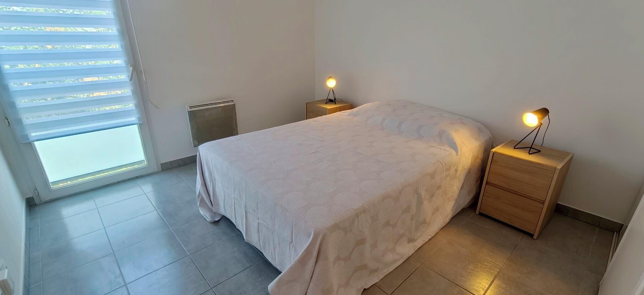 Ein Schlafzimmer mit einem Bett, zwei Nachttischen, einem Heizgerät und einem Fenster mit Jalousien.