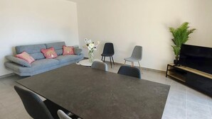Uma sala de estar com um sofá cinzento, uma mesa de centro, um rack para TV e uma planta em vaso.